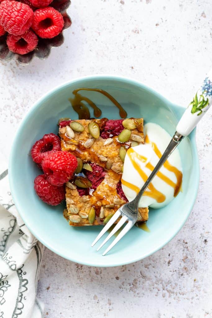 Slice of baked oats served in a bowl with raspberries and yogurt