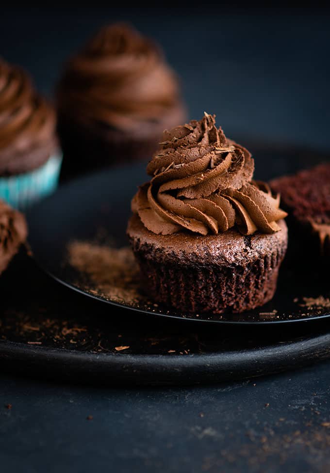 Vegan chocolate cupcakes topped with vegan ganache and chocolate shavings on a plate