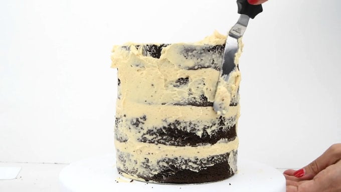 Adding frosting to the sides of a salted caramel cake with an offset spatula