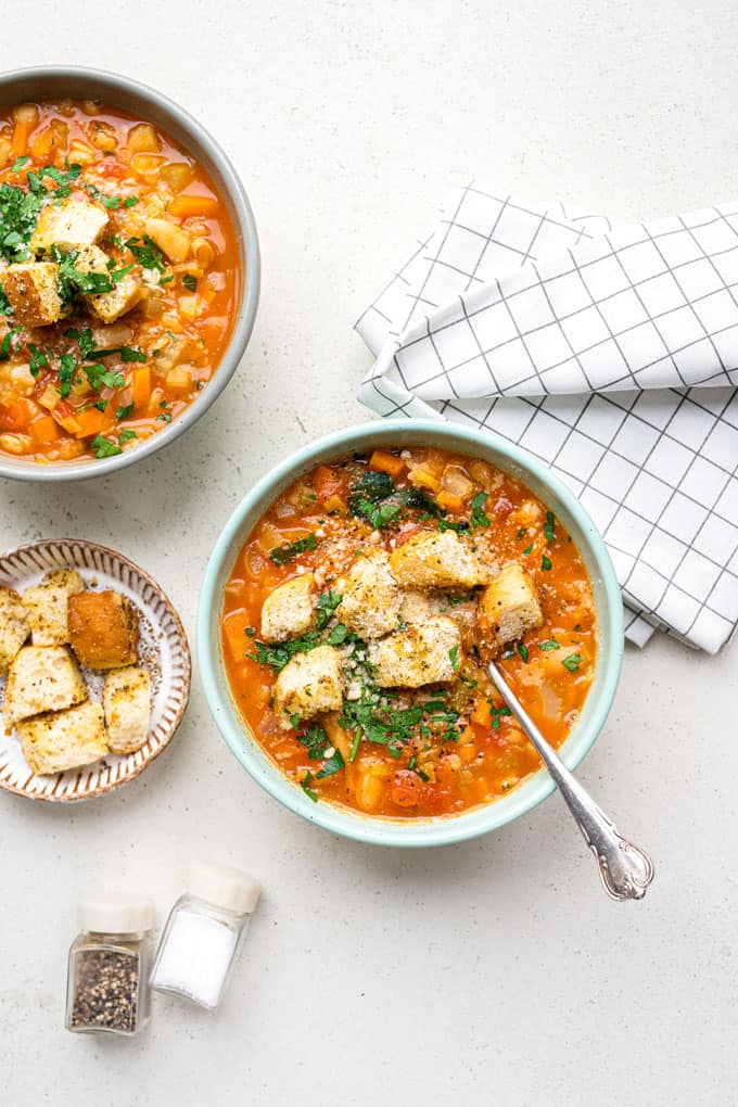 Two bowls of minestrone with croutons, parsley and grated parmesan