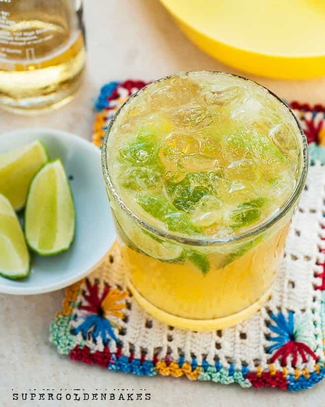 Beergarita cocktail topped with ice in a glass with lime wedges on the side