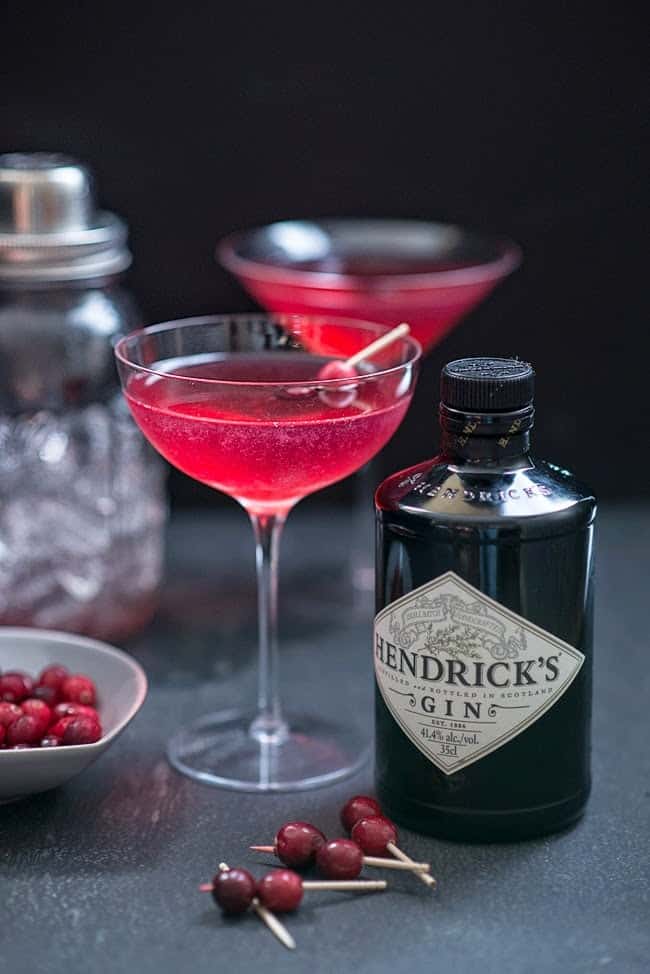 Red Queen cocktail with cranberry garnish and bottle of Hendricks Gin on the side
