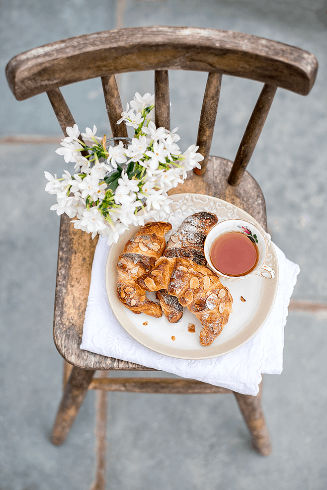 plate with almond croissants and a cup of tea on a rustic chair