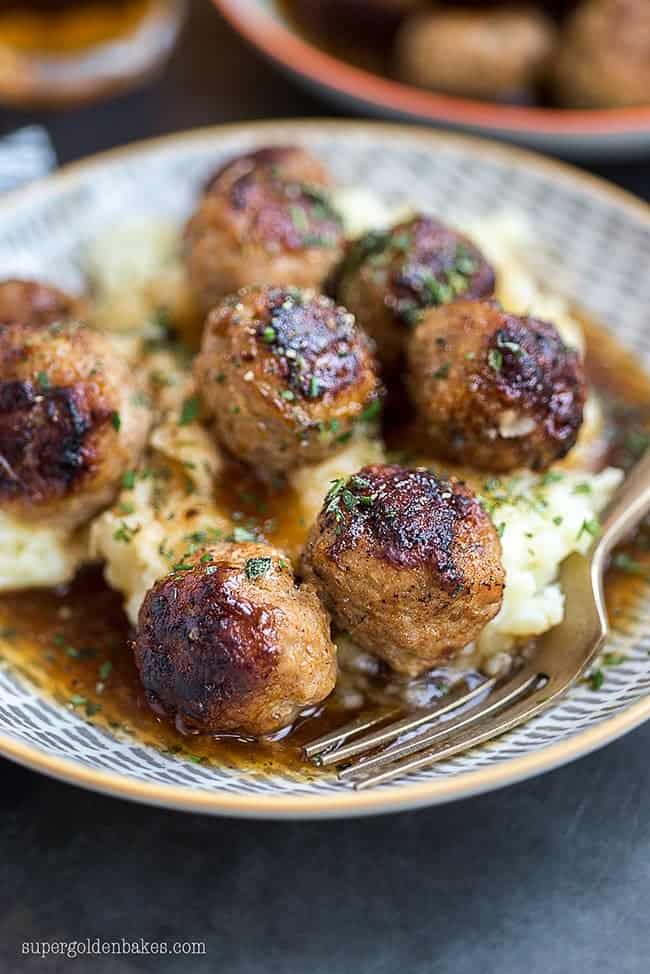 Close up on a bowl of meatballs and gravy served over mashed potatoes