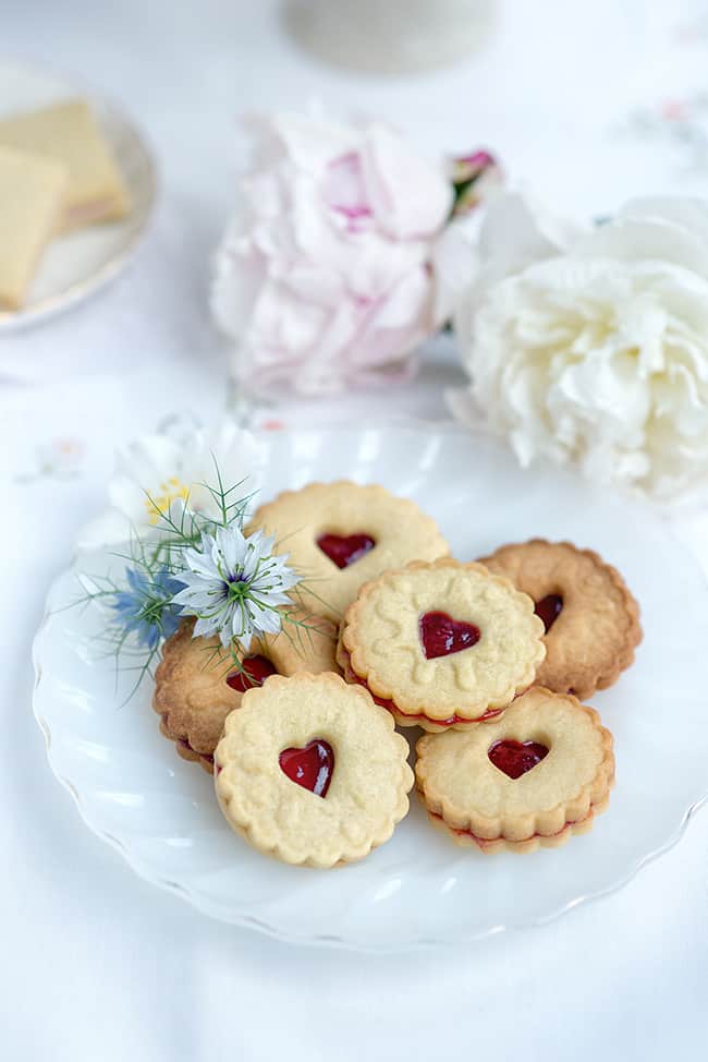 homemade Jammy Dodger biscuits sandwiched with seedless raspberry jam on a pretty plate with flowers on the side
