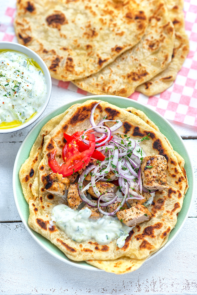 Pork souvlaki meat served with tzatziki, onions and tomatoes on pita bread on a green plate