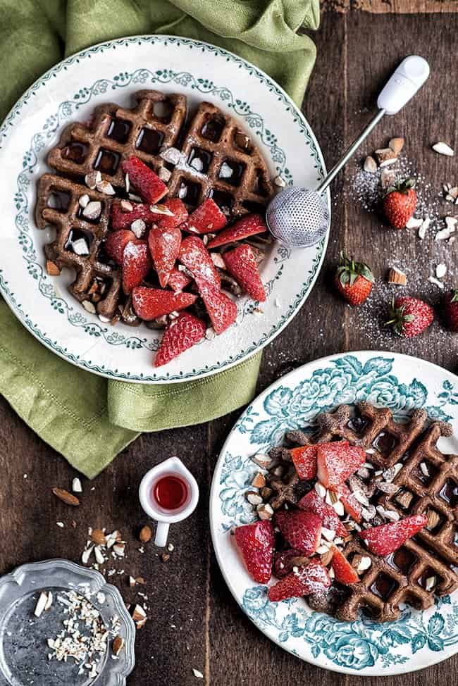 Waffles with sliced strawberries and chopped almonds on two patterned plates