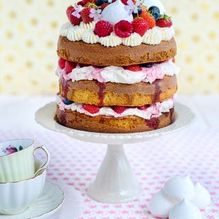 Eton mess Cake on a cake stand decorated with fresh berries and mini meringues