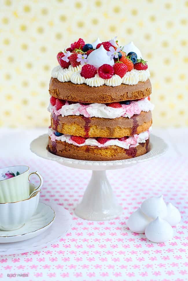 Eton mess Cake on a cake stand decorated with fresh berries and mini meringues