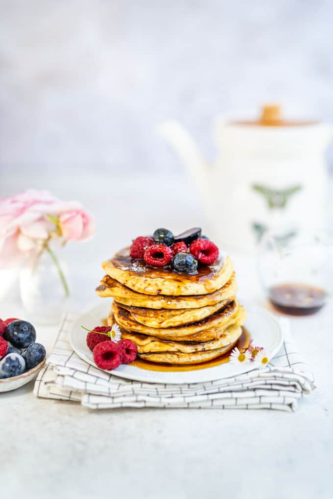 Stack of American Pancakes topped with blueberries and raspberries and drizzled with maple syrup