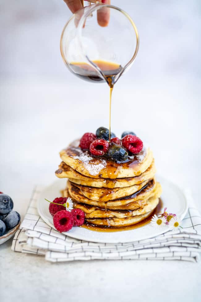 American pancakes stacked on a plate topped with berries and drizzled with maple syrup