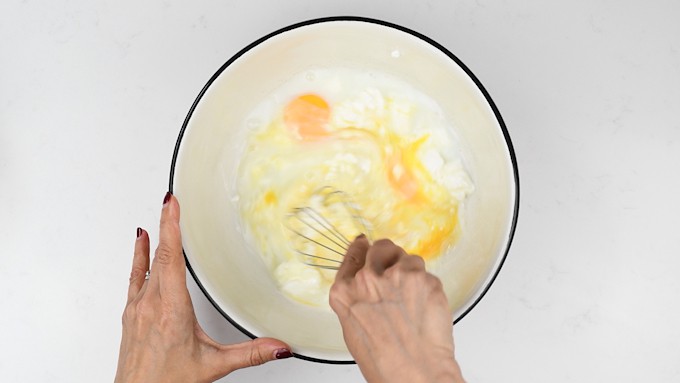 mixing eggs, quark cheese and milk in a bowl with a hand whisk