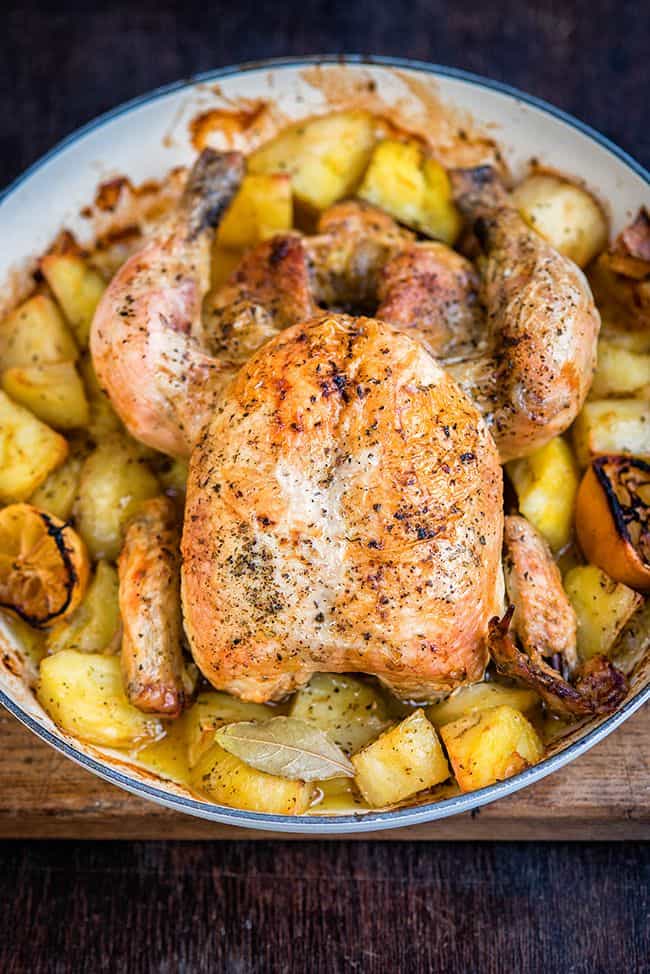 Close up of roast chicken In a pan with potatoes lemons and bay leaves