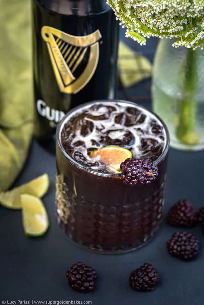 Guinness cocktail in a rocks glass with blackberries and lime wedge