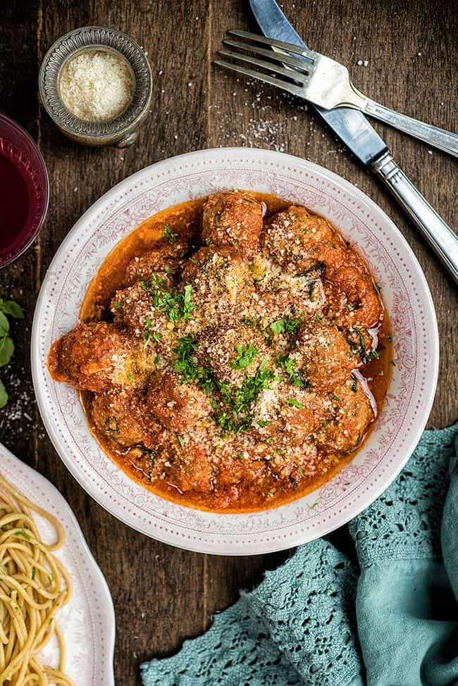 Bowl of beef meatballs in tomato sauce garnished with basil and Parmesan