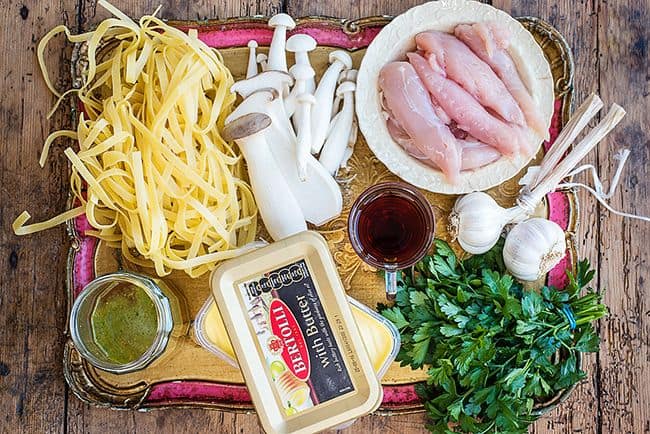 Ingredients for pasta with chicken and mushrooms arranged on a rustic tray
