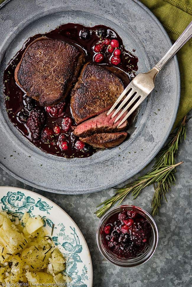Sliced venison steak with port and berry sauce on a metal plate