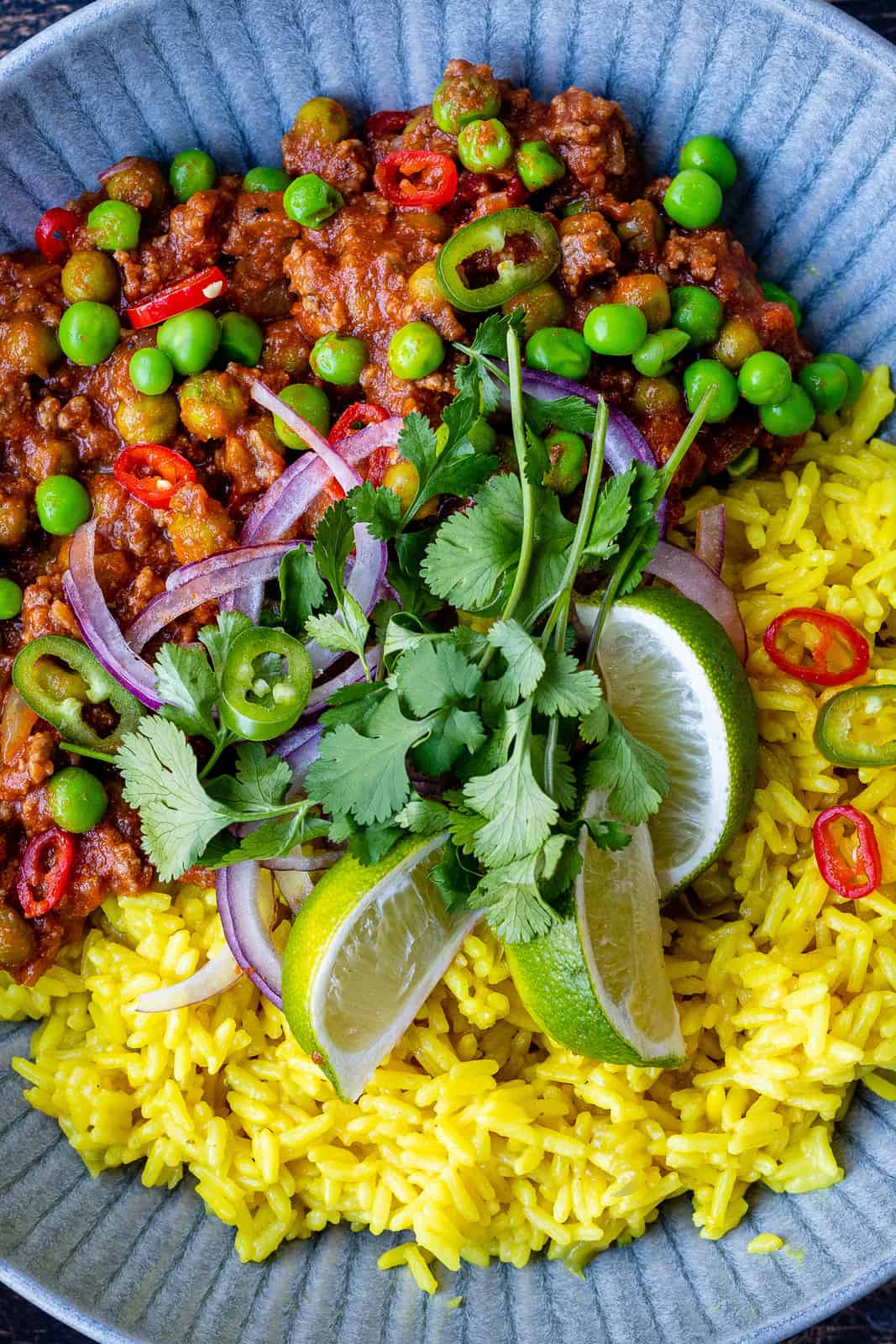 Close up on a bowl with pilau rice and beef keema curry garnished with coriander, red onion slices and lime slices