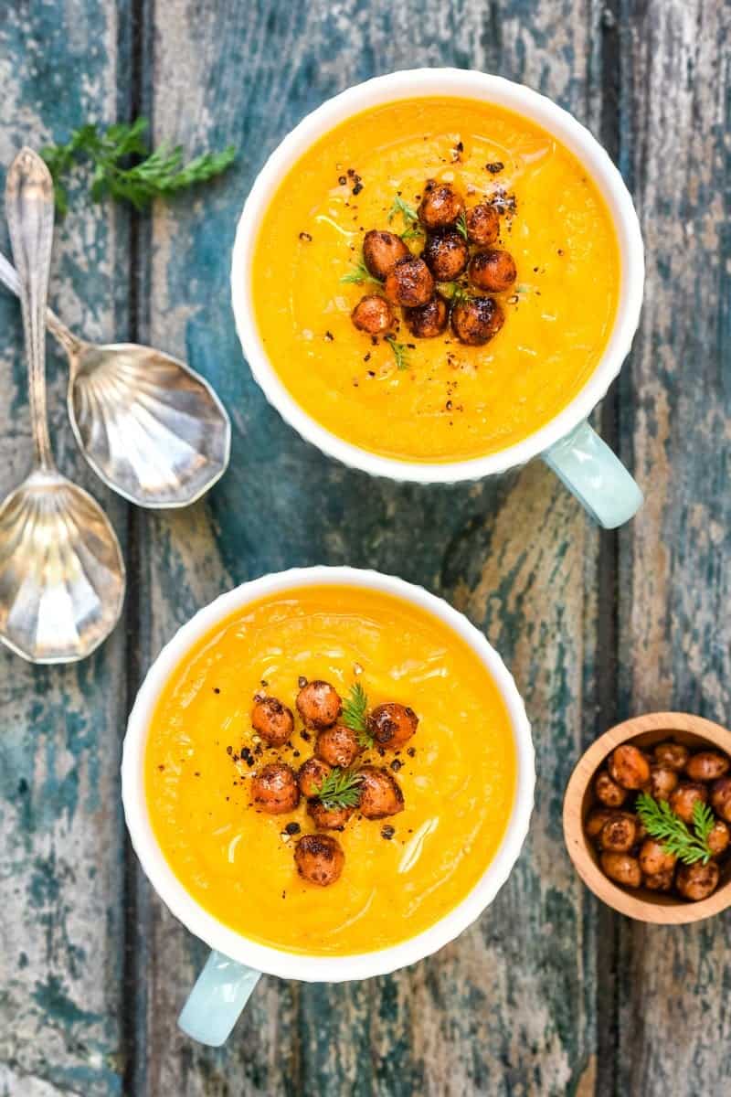 two mugs of carrot soup with chickpea garnish