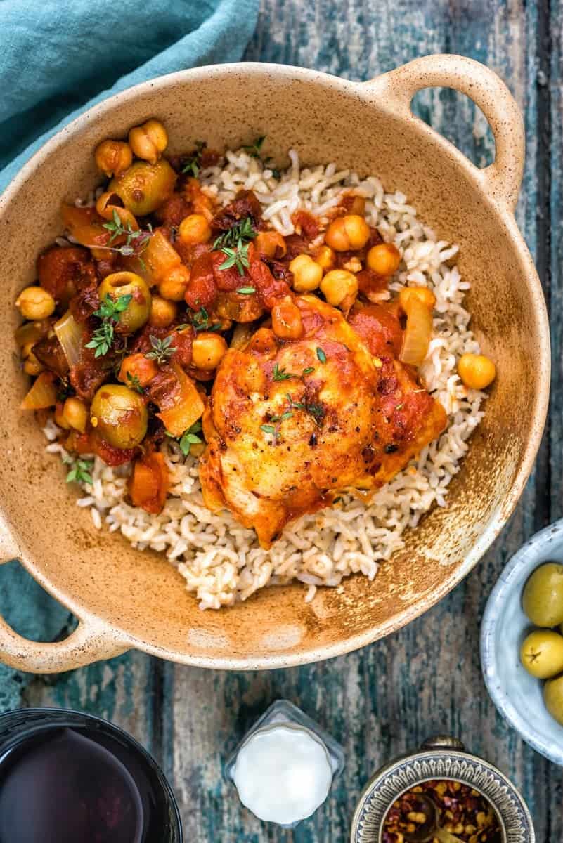 Chicken, chorizo, olive and chickpea stew served over rice in a rustic bowl