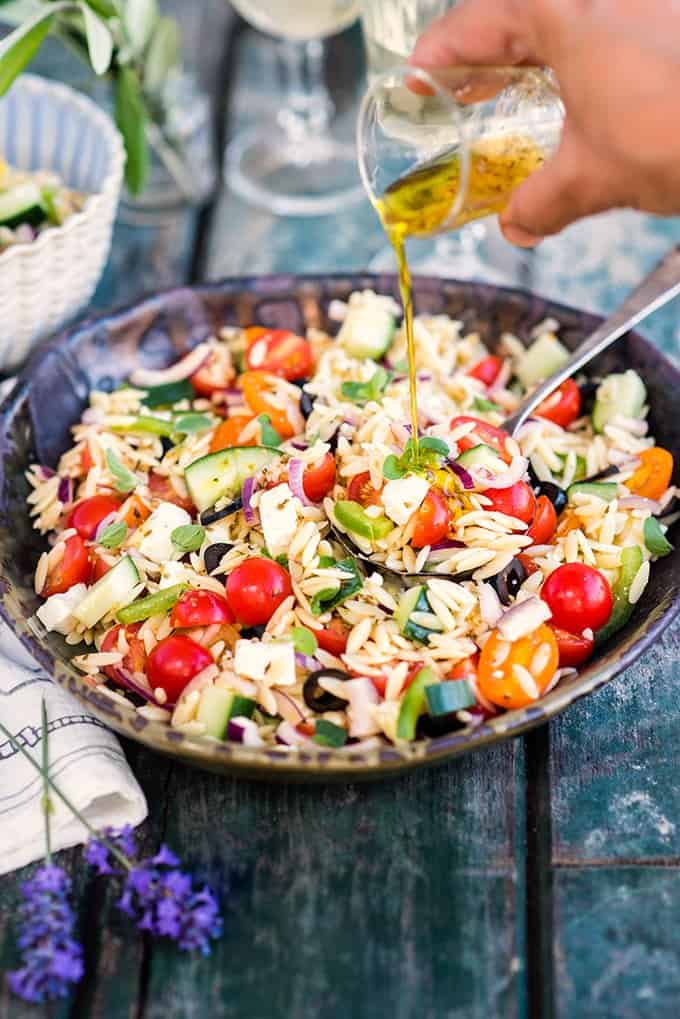 Greek Pasta Salad in a bowl being drizzled with marinade