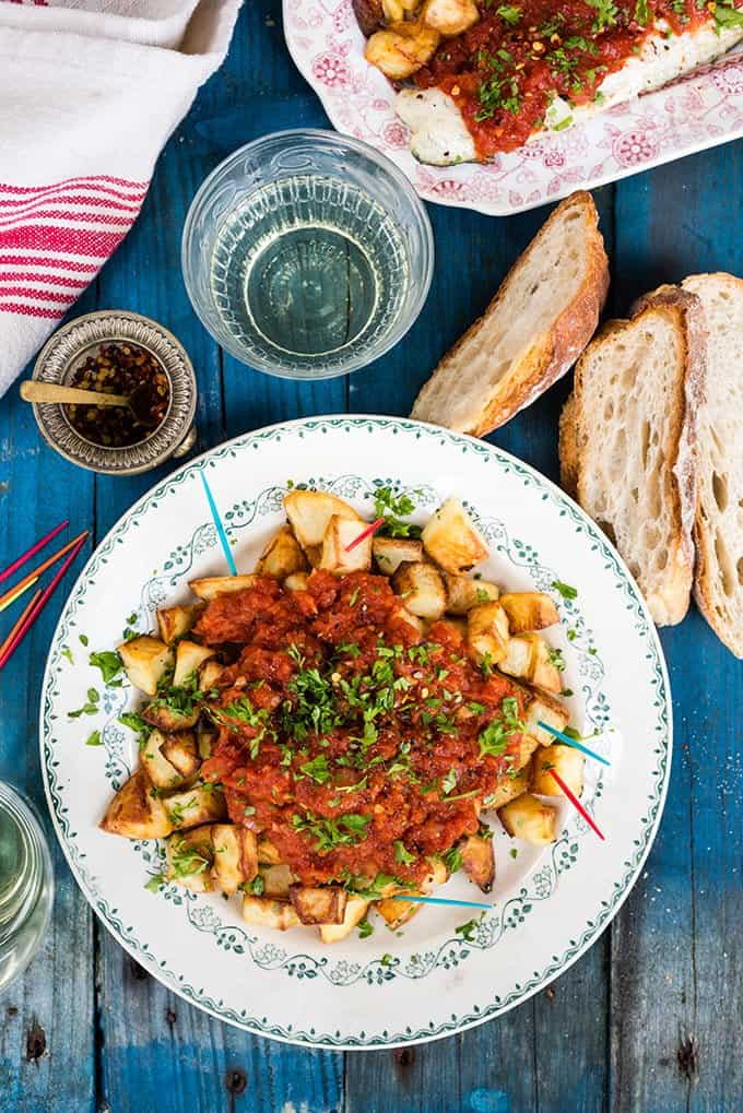 Summery Spanish oven-baked patatas bravas with seas bass. The potatoes make a great starter to share or turn them into a main with the fish.