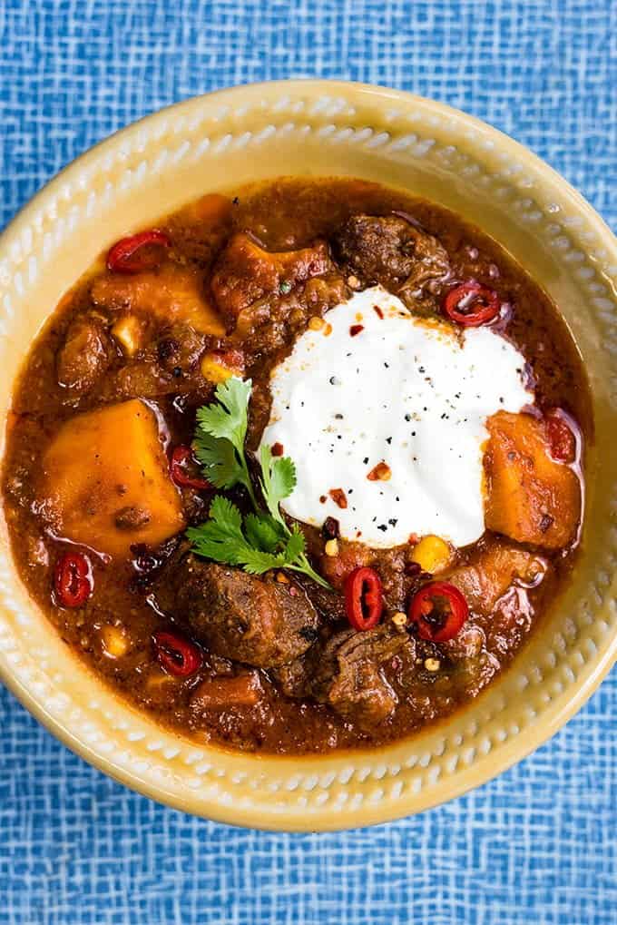 Bowl of beef stew with sweet potatoes garnished with sliced chilli and sour cream