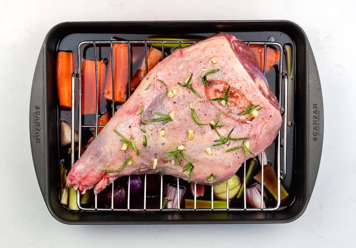 Leg of lamb on a roasting rack over vegetables in tray