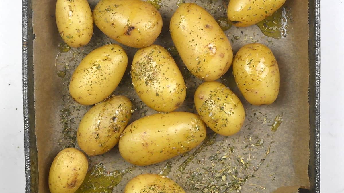 Potatoes seasoned with salt, pepper, herbs and olive oil in a roasting tin