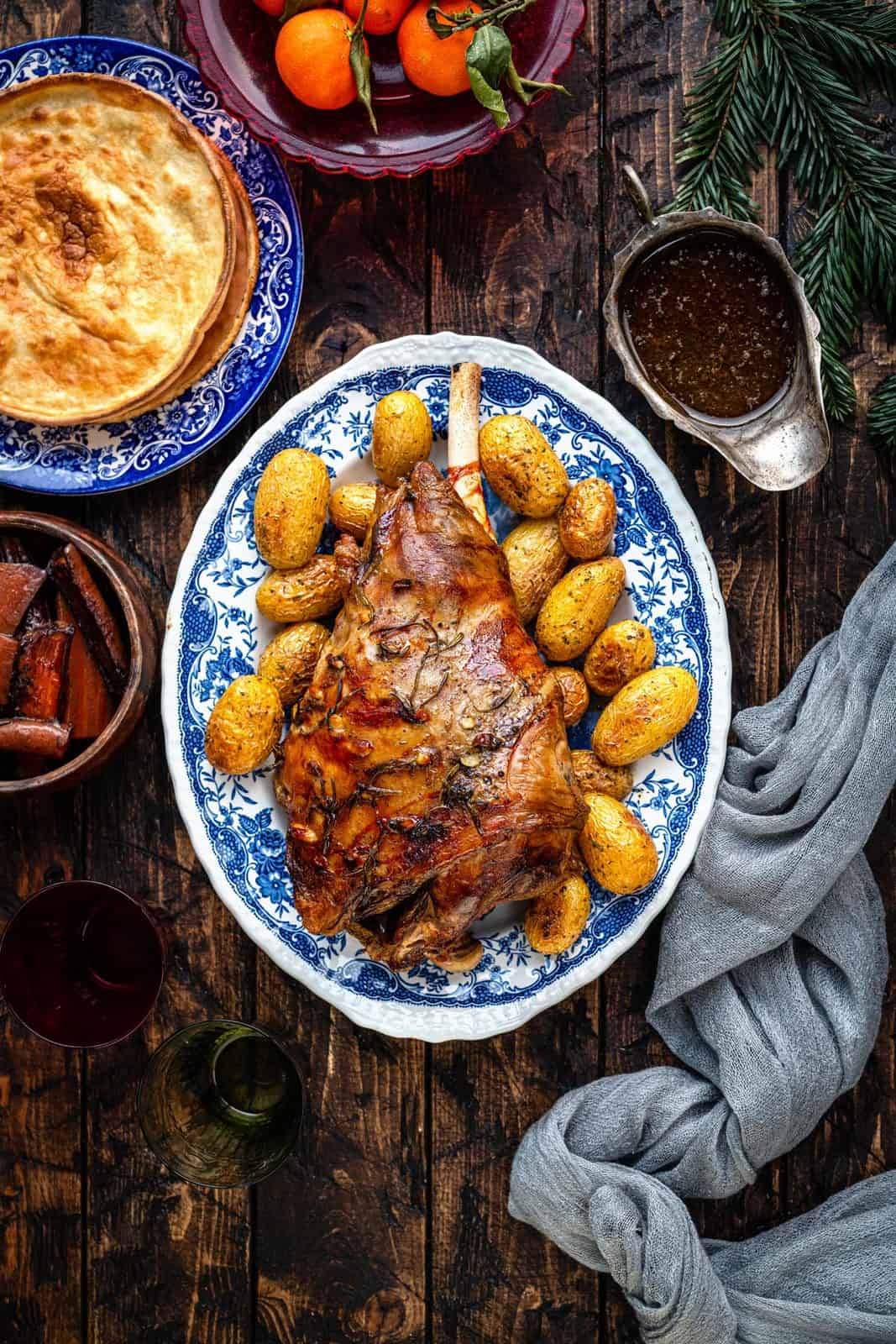Slow cooked leg of lamb on a platter with roast potatoes 