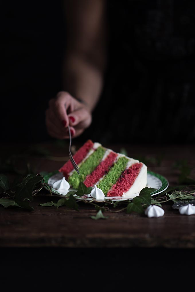 A showstopping Christmas layer cake filled with cranberry compote, whipped mascarpone frosting and crowned with a sweet meringue wreath. Slice to reveal the festive red and green layers! #Christmas #layercake #festivecake #rainbowcake