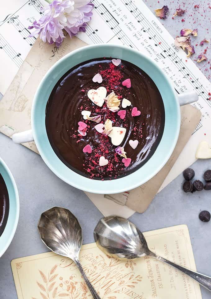 Garnishing chocolate soup with heart-shaped sprinkles, raspberry powder and rose petals