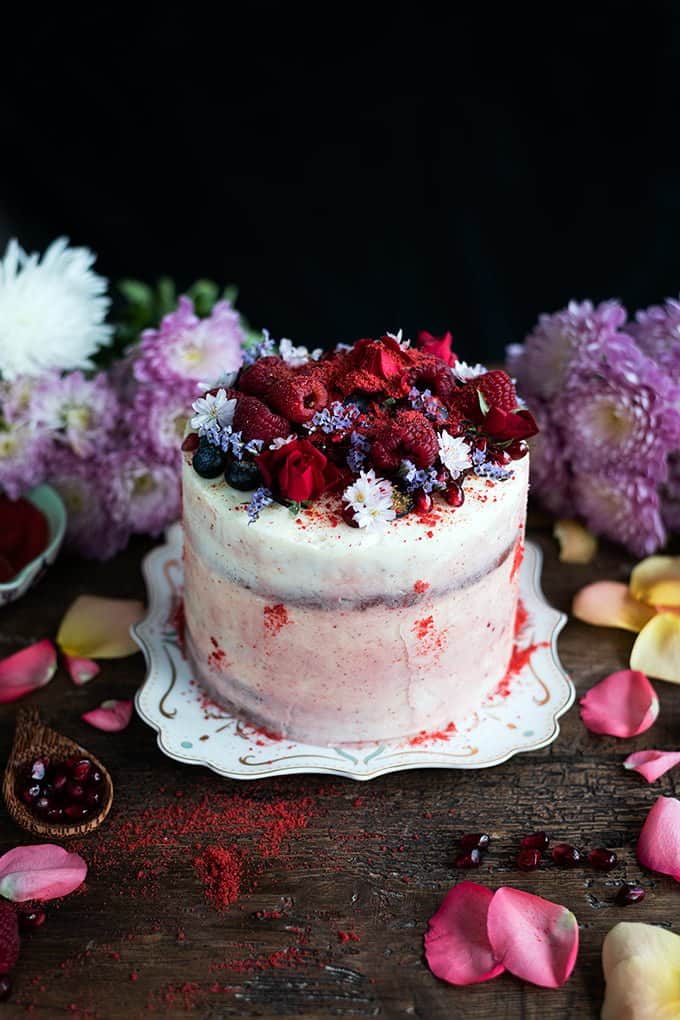 red velvet layer cake is sandwiched with vanilla and strawberry frosting and decorated with a medley of berries and flowers