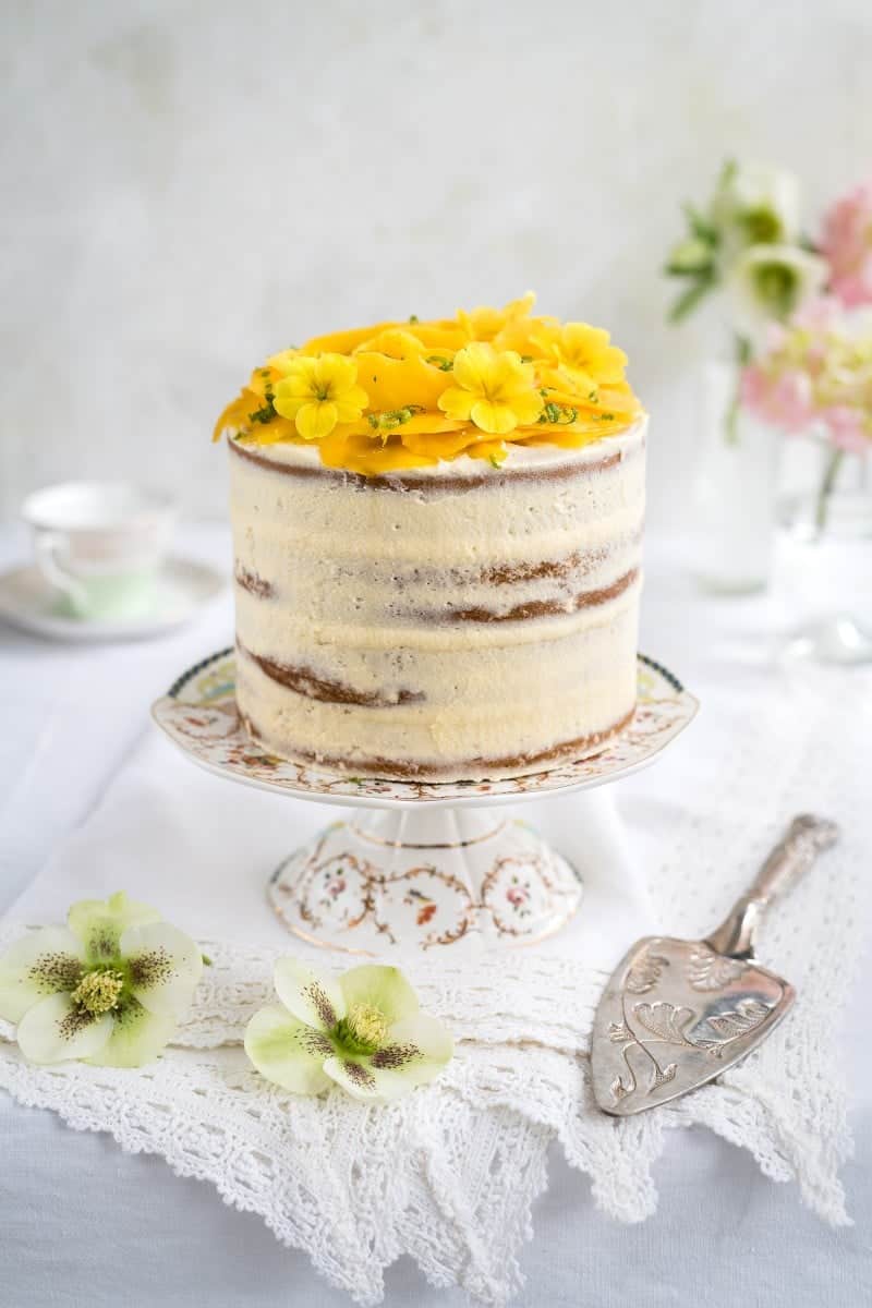Tall vegan layer cake topped with a mango rose and edible flowers