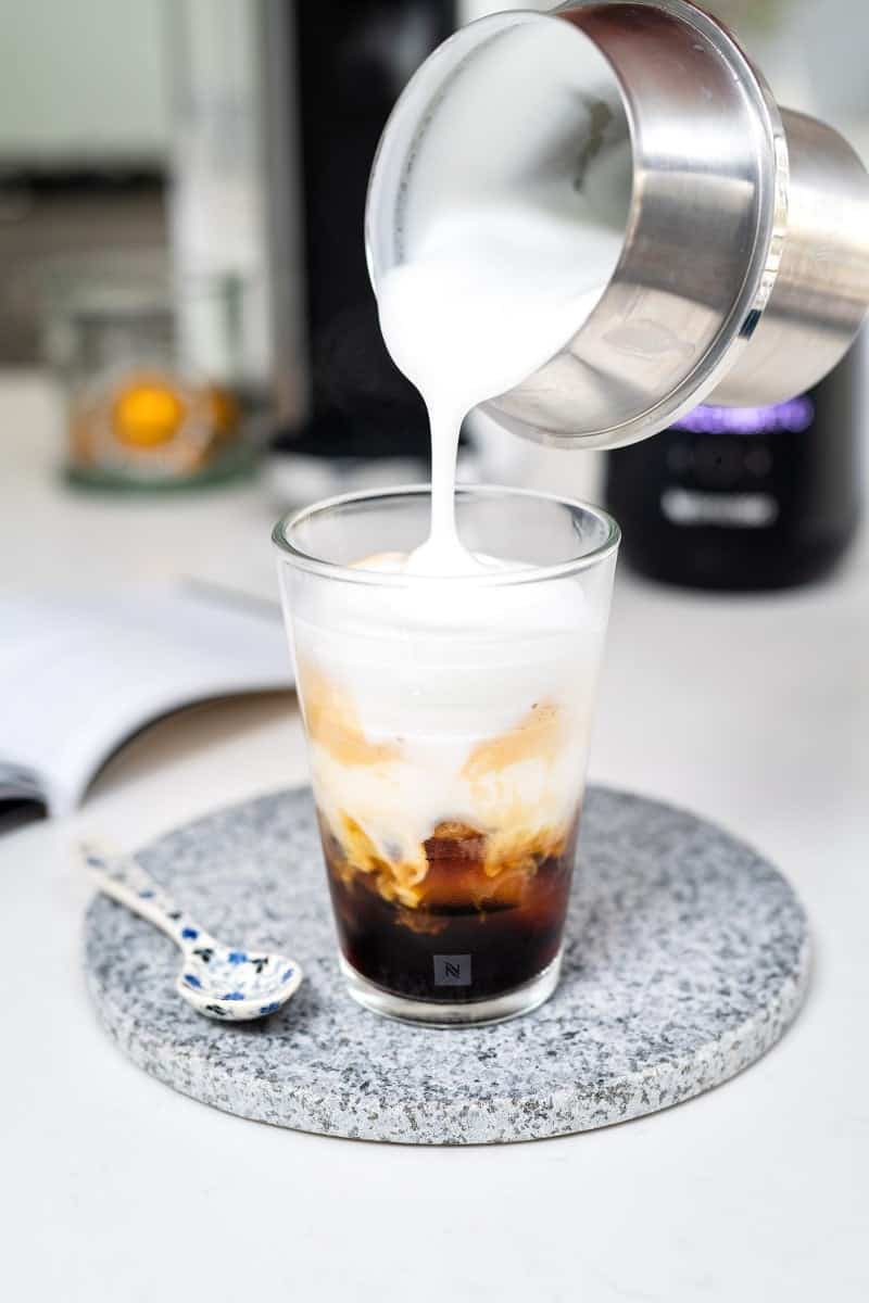 Pouring milk foam onto a glass of Nespresso on Ice Macchiato