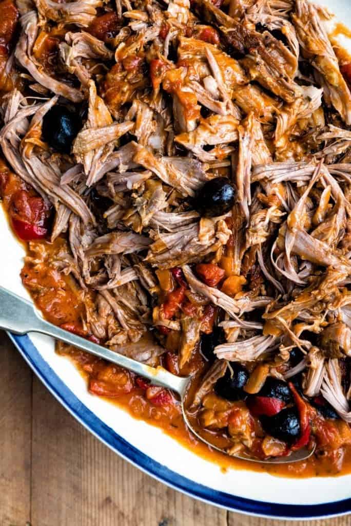 Close up on a platter of pulled lamb in rich tomato sauce with black olives
