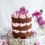 Chocolate layer cake on a cake tin, frosted with Italian buttercream and decorated with lilacs