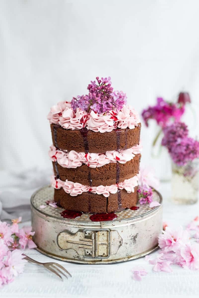 Chocolate layer cake on a cake tin, frosted with Italian buttercream and decorated with lilacs