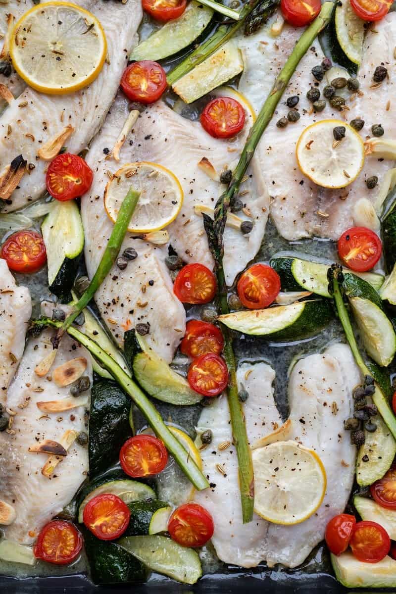 Oven-baked tilapia on a sheet pan with vegetables and tomatoes