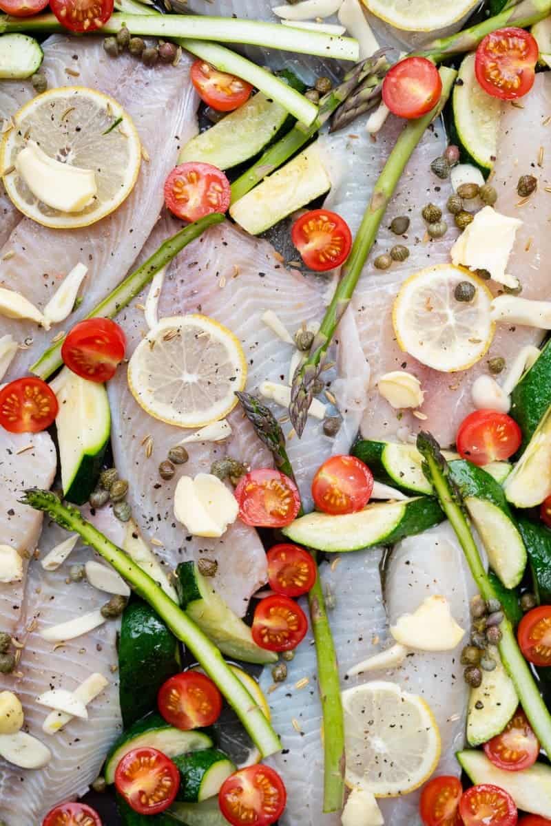 Tilapia arranged on a sheet pan with vegetables ready for the oven