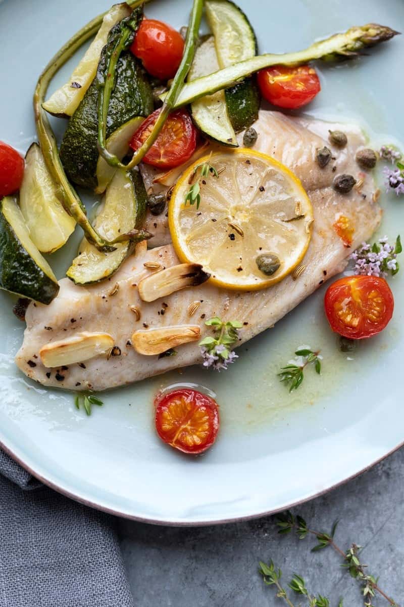 Plated baked tilapia with vegetables, lemon and capers