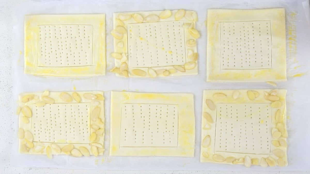 Brushing puff pastry with egg wash and adding flaked almonds