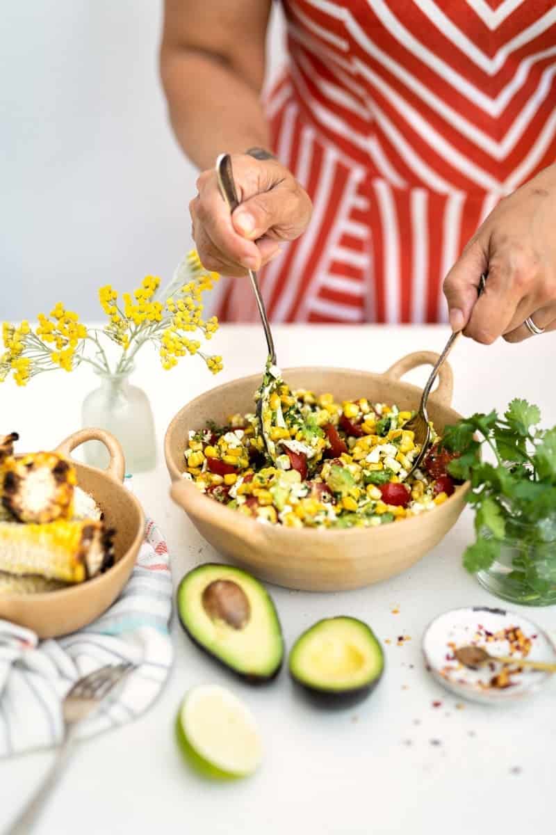 Mixing grilled corn, feta and avocado salad in a bowl