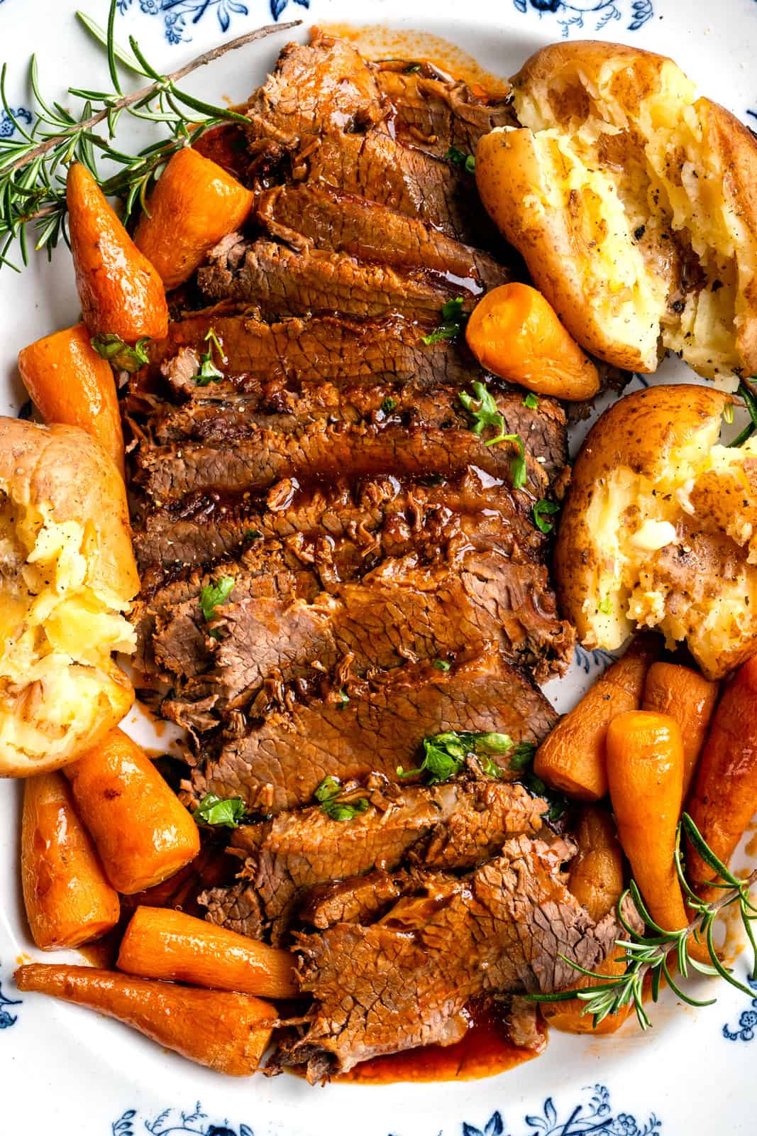 Close up on a platter of slices brisket served with carrots, potatoes and gravy