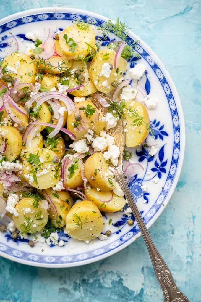 Close up on a plate of Greek potato salad with feta, onions, capers and herbs