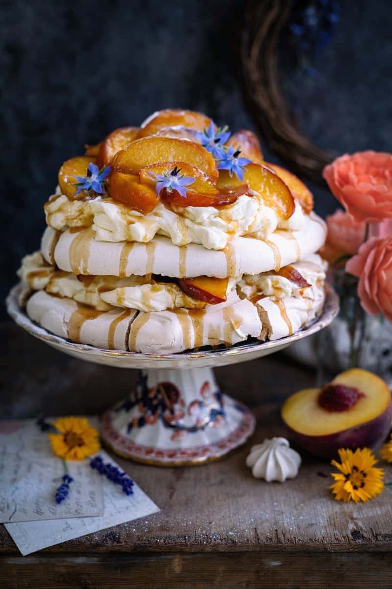 Brown sugar layered pavlova with caramelised peaches on a cake stand decorated with flowers