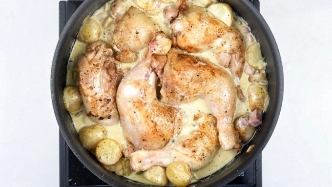 Chicken legs nestled among potatoes and cream in a large pan