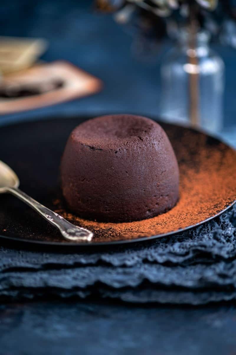 Molten lava cake on a black plate dusted with cocoa powder