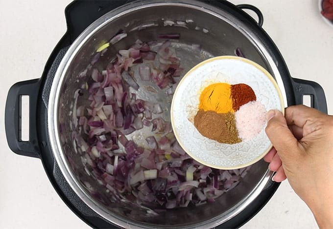 Adding spices to cooked onions in a pot