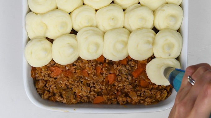 Piping mashed potatoes over traditional Shepherd's pie